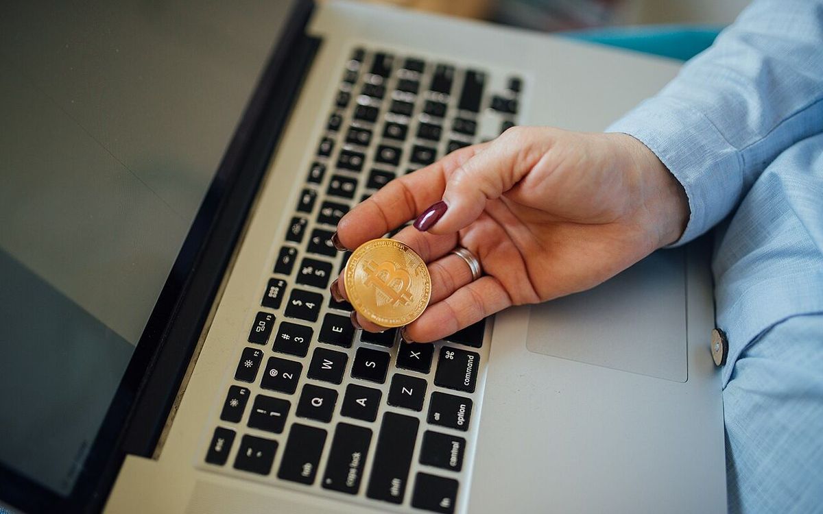 Close-up of a Bitcoin physical coin in a womans hand and a laptop on her lap